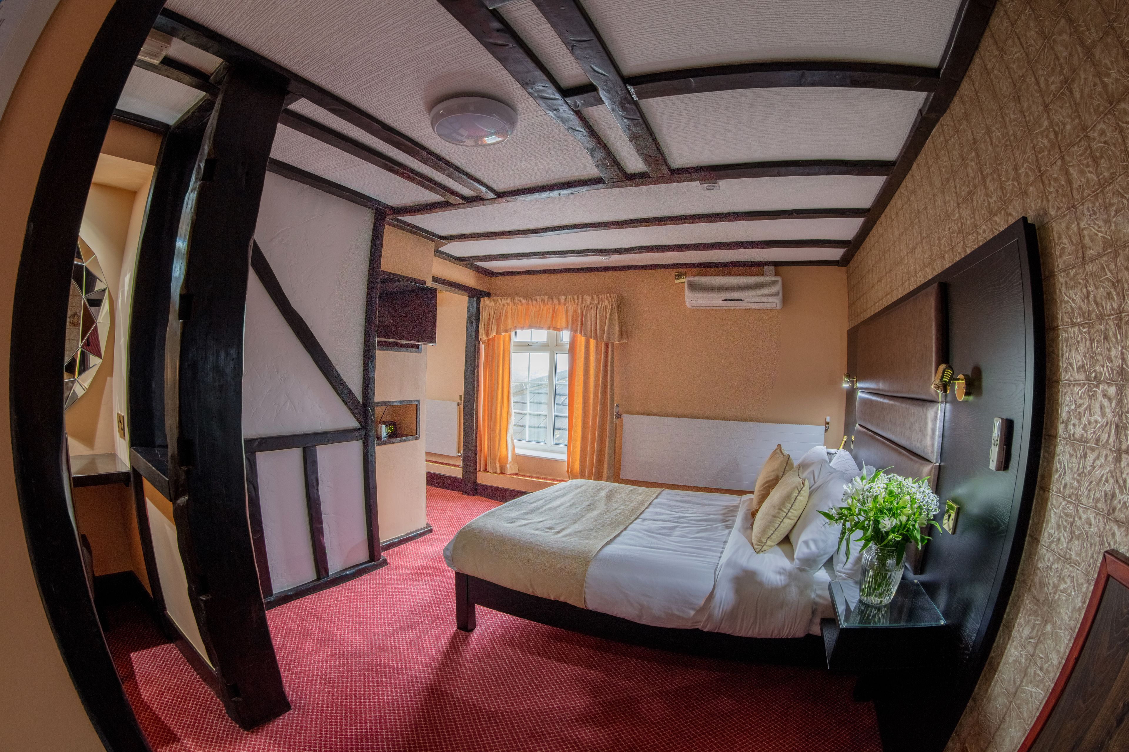 A room with a bed, a nightstand, a window with curtains, a wall-mounted air conditioner, and a door leading to another room.