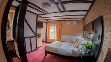A room with a bed, a nightstand, a window with curtains, a wall-mounted air conditioner, and a door leading to another room.