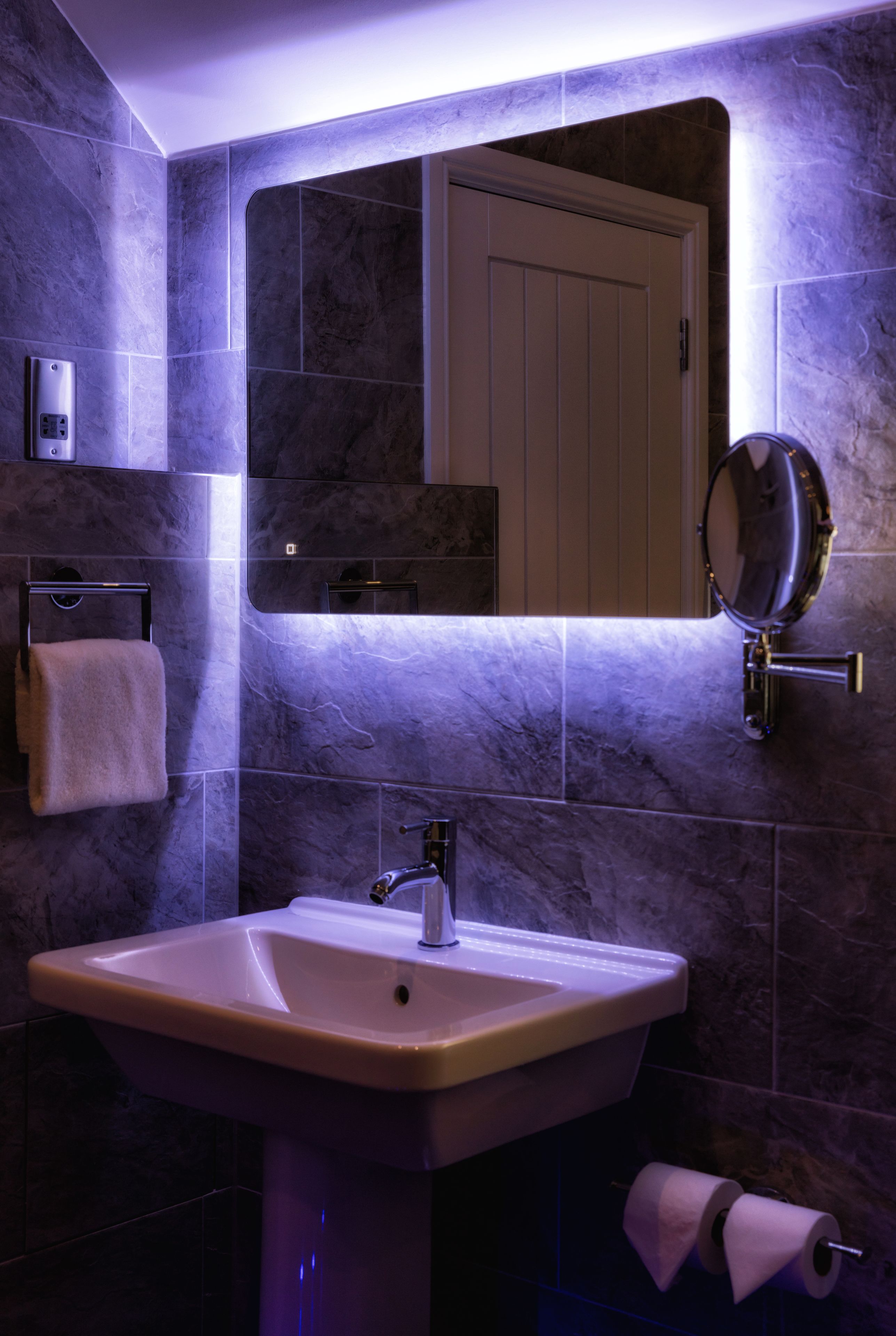 A bathroom with a sink, mirror, towel rack, and toilet paper dispenser.