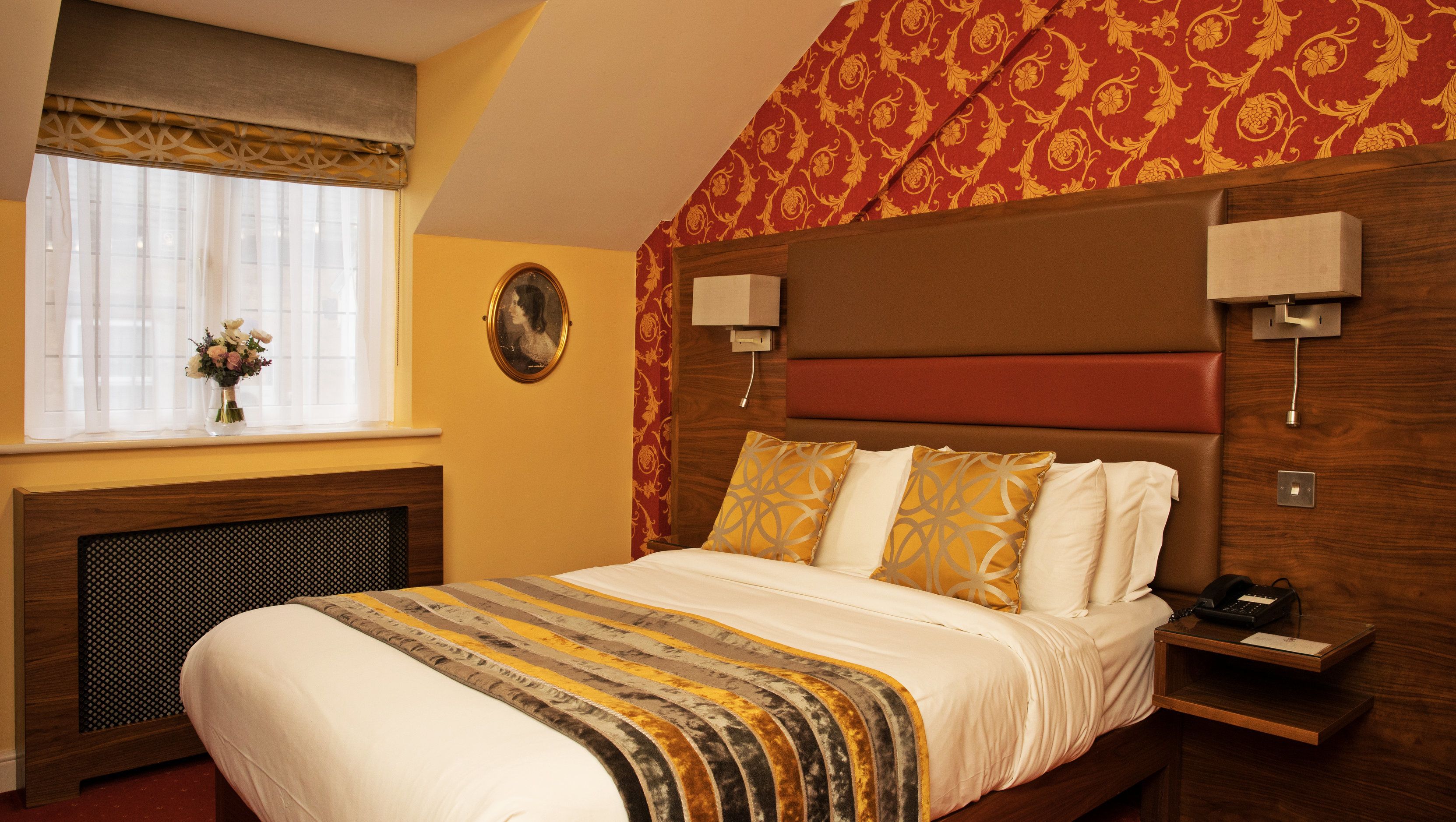 A hotel room with a bed, bedside table, and a window with curtains.