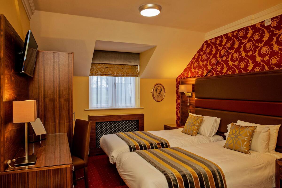 A hotel room with a bed, bedside table, lamp, and a TV mounted on the wall.