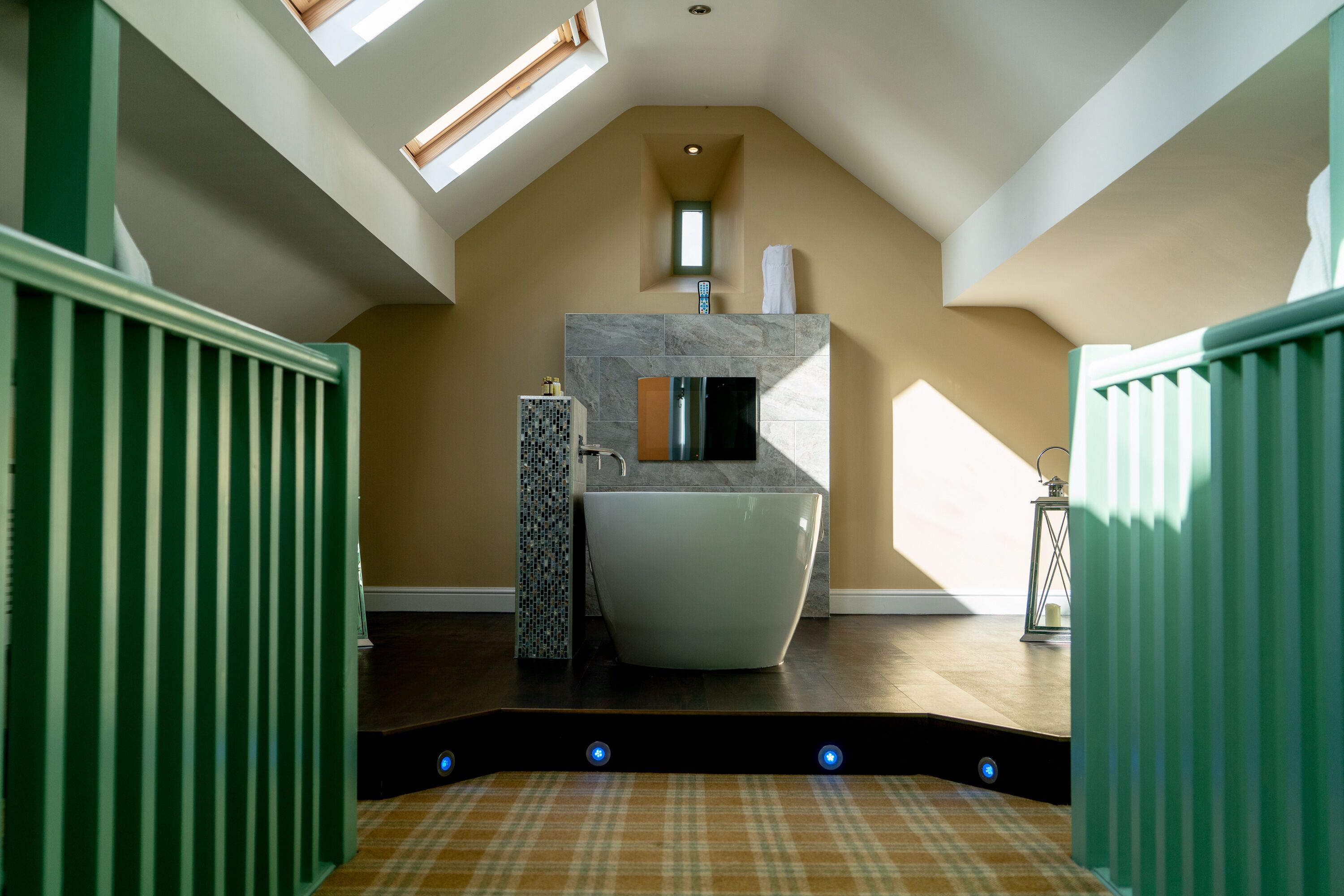 A modern bathroom with a freestanding bathtub, a small window, and a green railing.