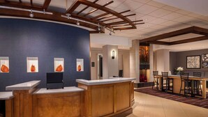 A hotel reception area with a curved reception desk, a seating area with a bar, and a wall with framed pictures. - Hyatt Place Mt Laurel (Mount Laurel)