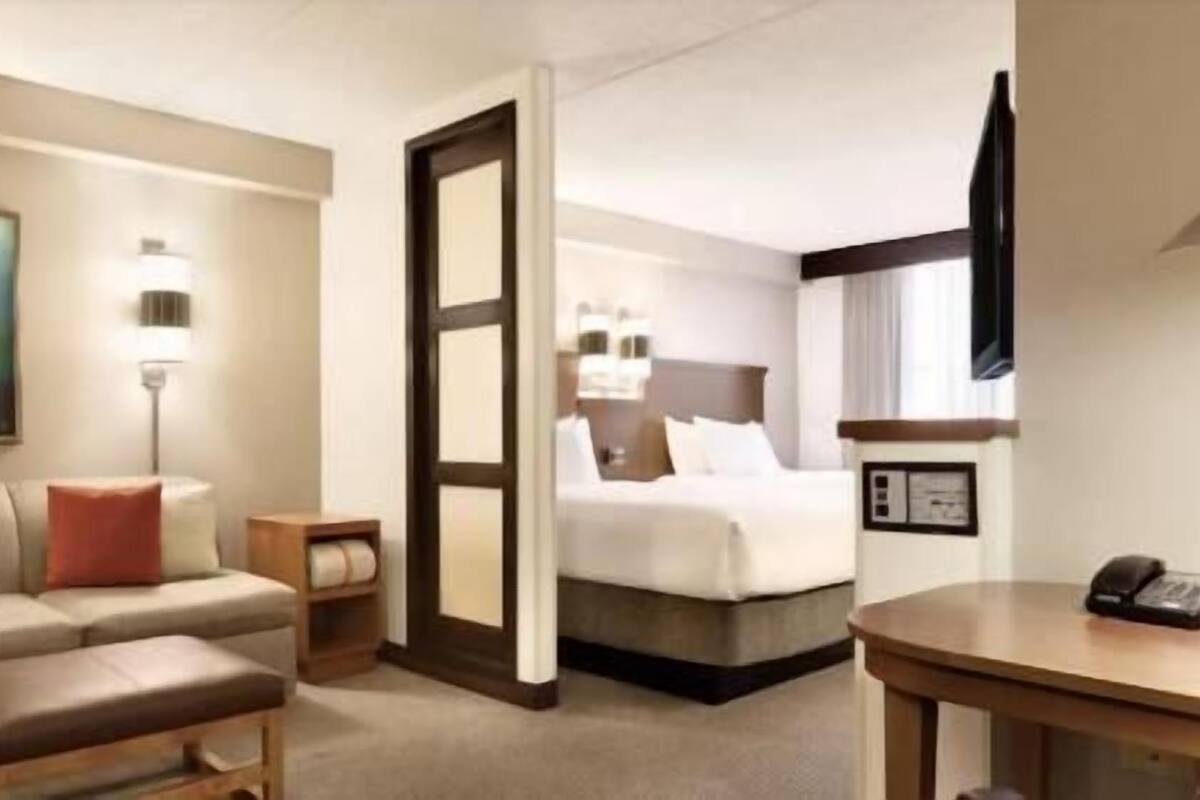 A hotel room with a bed, a sofa, a small table, a TV, and a painting on the wall.
