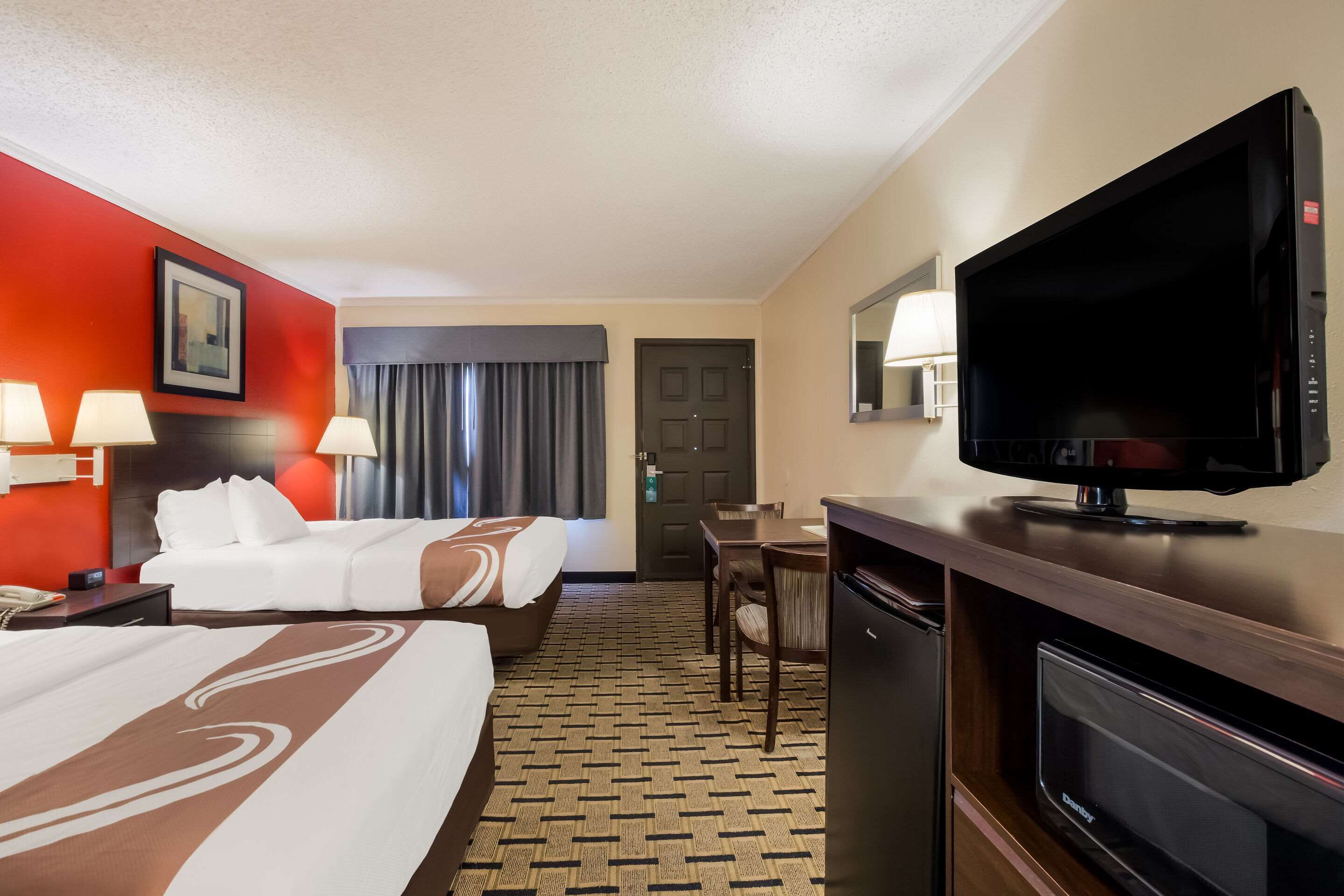 A hotel room with two beds, a TV, a desk, and a minibar.