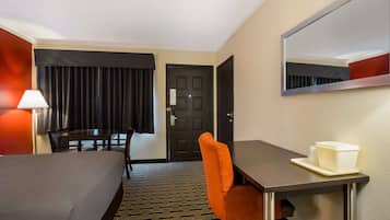 Une chambre d’hôtel avec un lit, un bureau, une chaise, une lampe, une porte et un miroir.