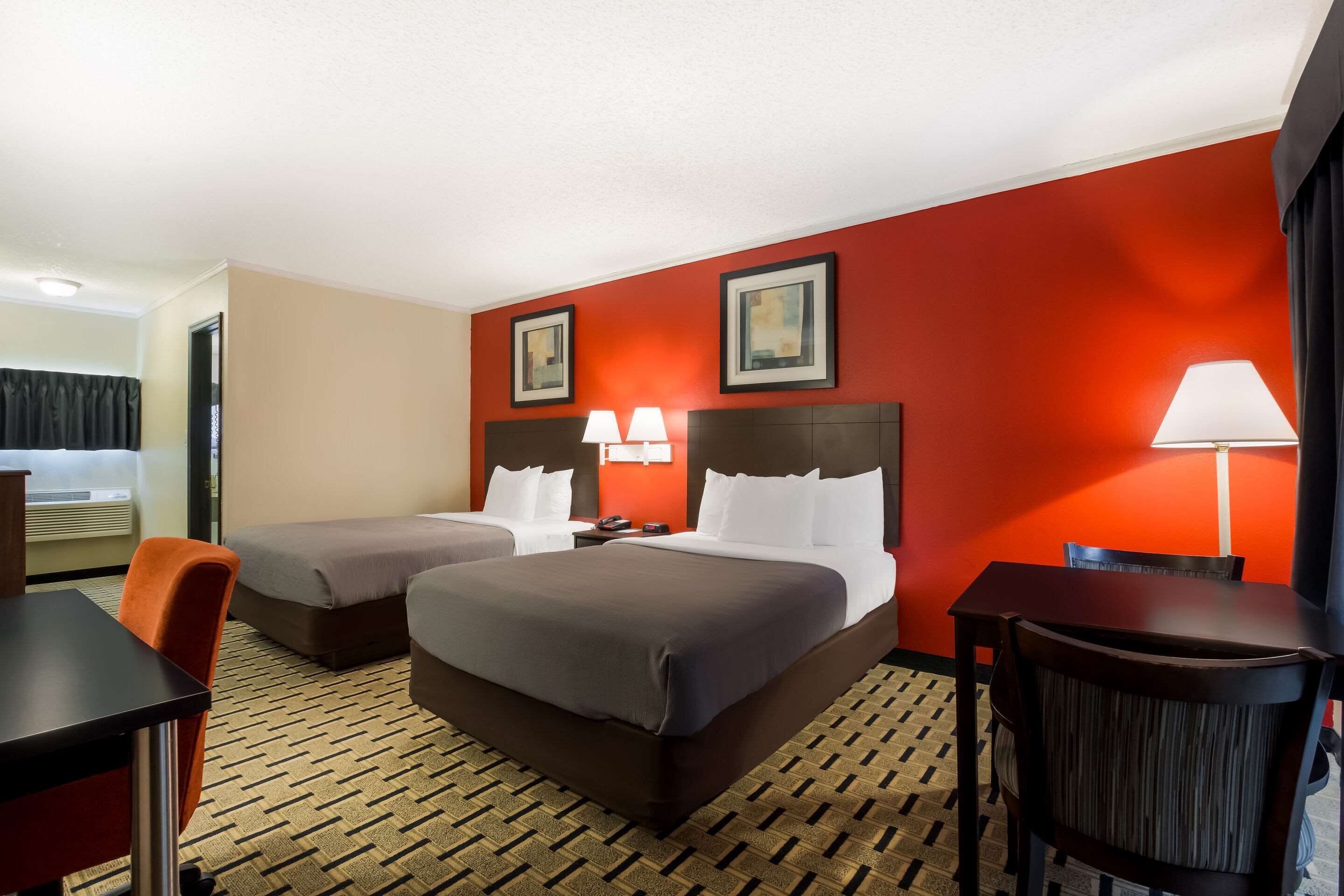 A hotel room with two beds, a desk, a chair, and a table.