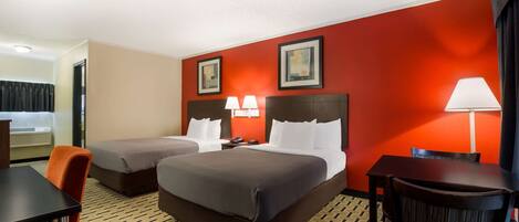 A hotel room with two beds, a desk, a chair, and a table.