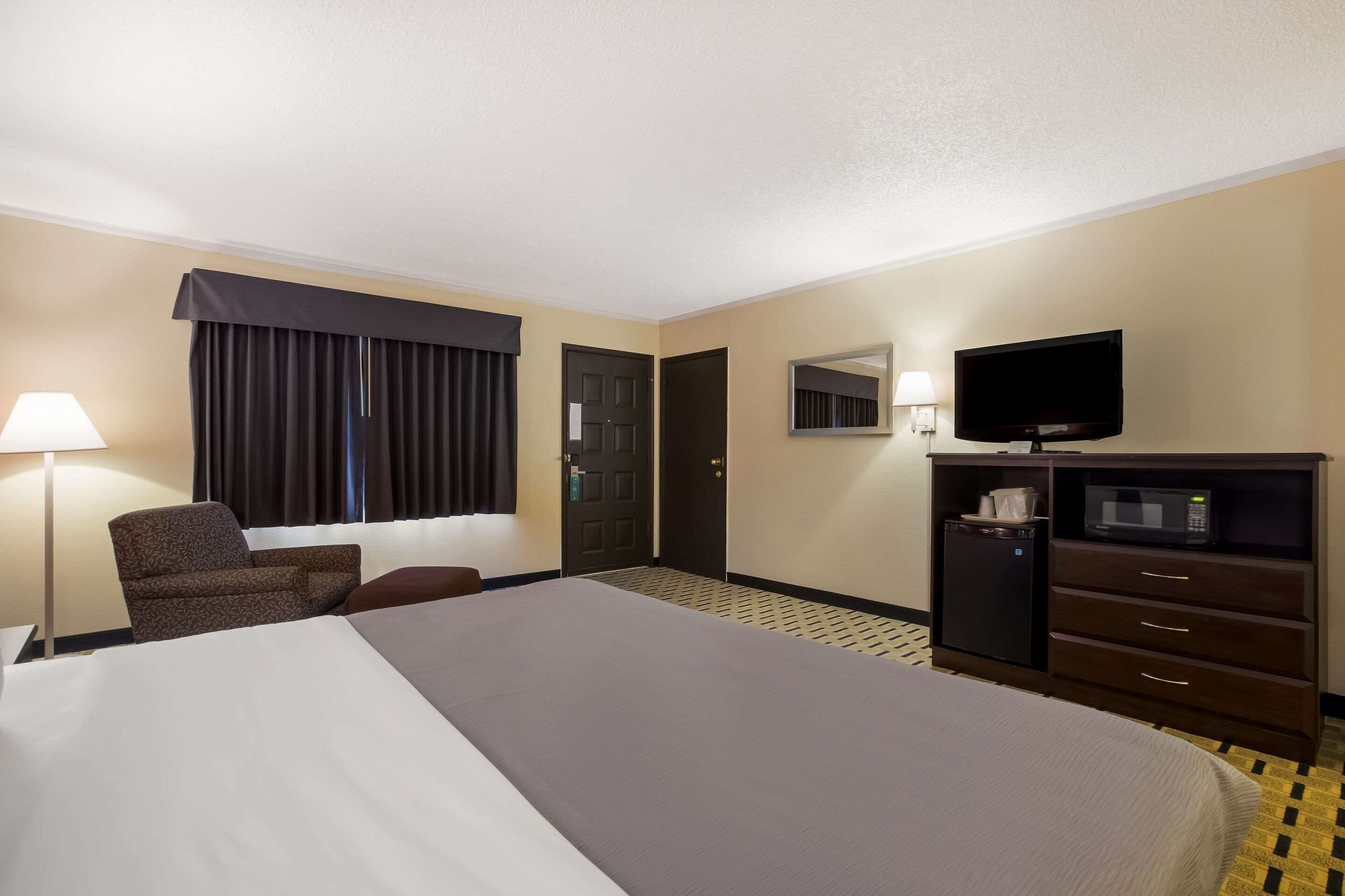 Une chambre d’hôtel avec un grand lit, une télévision, un minibar, une chaise et une porte donnant sur une autre chambre.