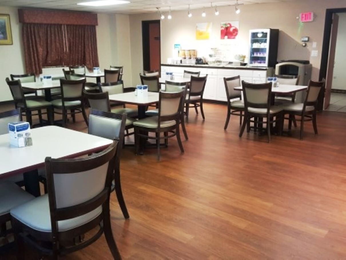 A dining area with multiple tables and chairs, a kitchen in the background, and an exit sign.