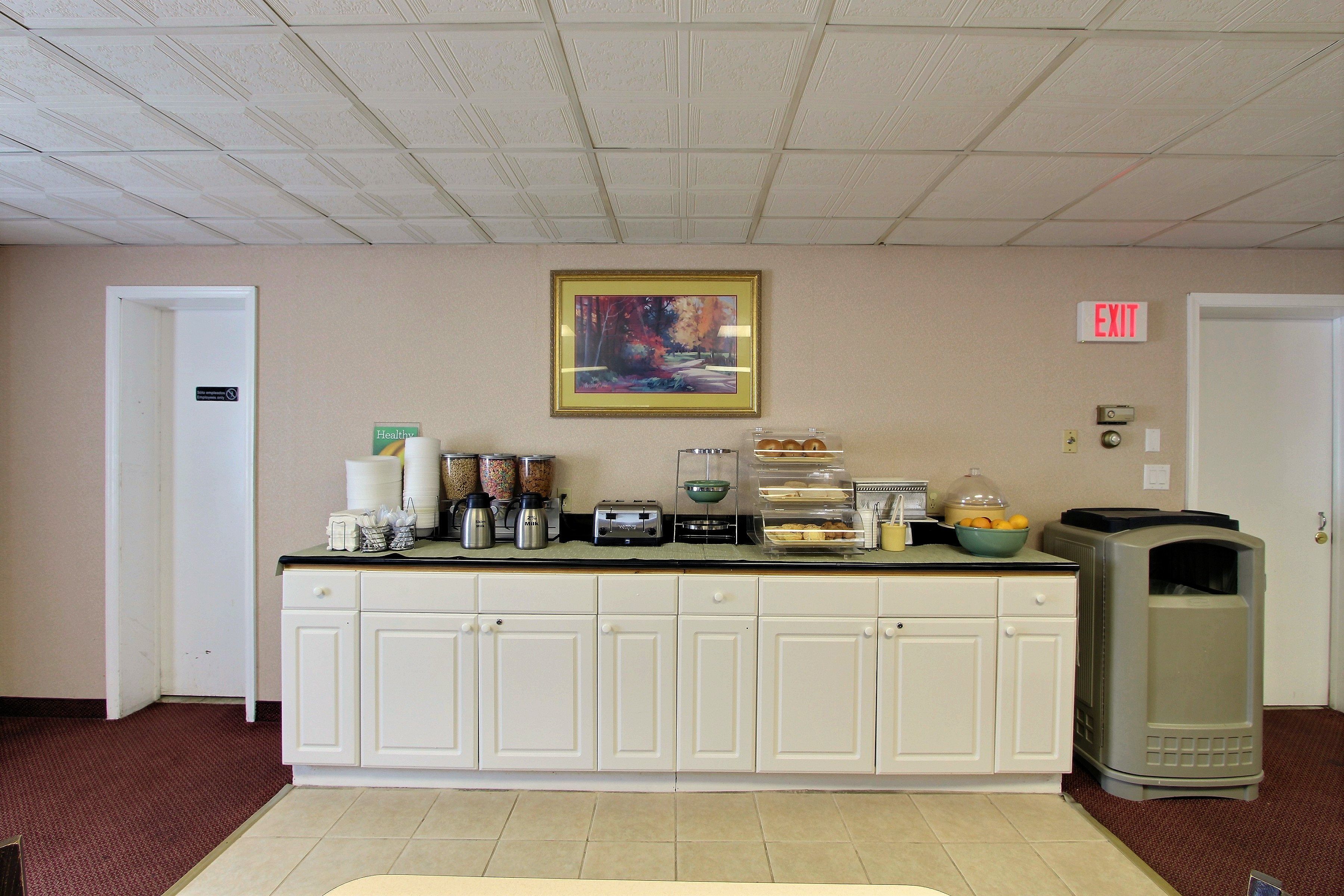 A kitchenette with a coffee maker, toaster, and various containers. There is a framed picture on the wall and an exit sign.
