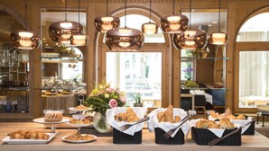 Un buffet de petit-déjeuner proposant diverses pâtisseries et assortiments de pains, un vase de fleurs et des lampes suspendues décoratives.