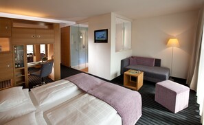 A hotel room with a bed, a desk, a chair, a sofa, and a small table with a magazine. - Hotel Ammerhauser (Anthering)
