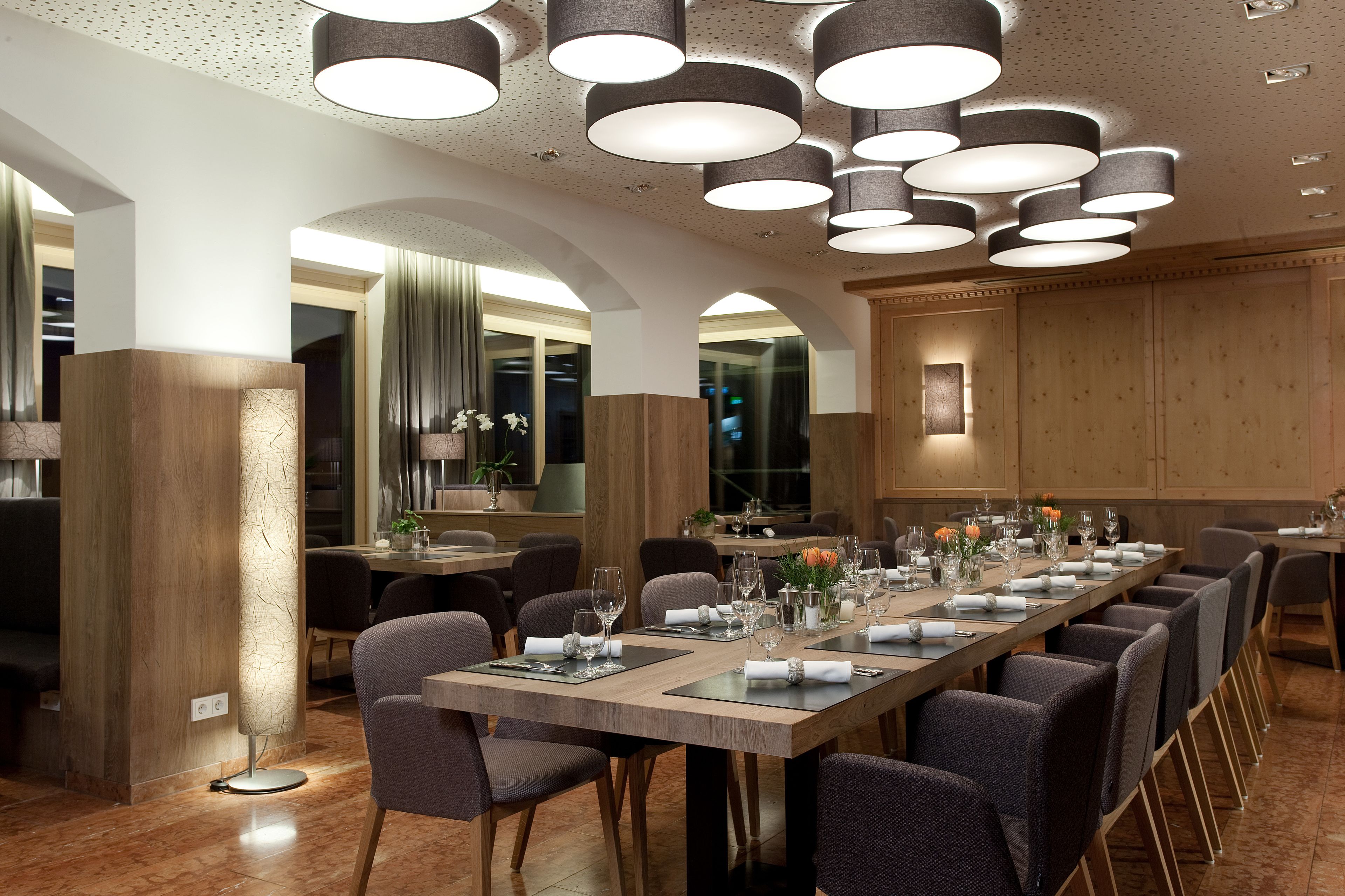 Une longue table à manger, entourée de chaises, agrémentée de plusieurs suspensions et dotée d’un aménagement intérieur moderne.