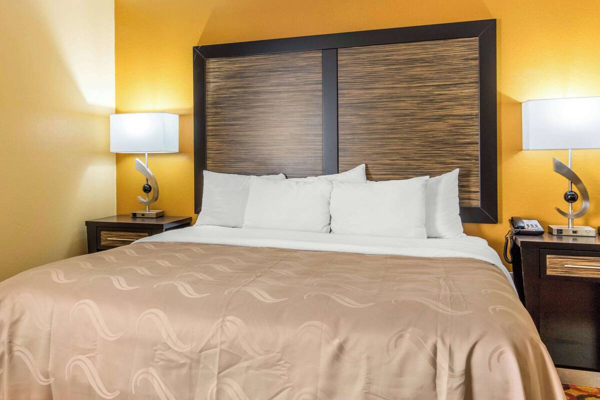 A hotel room with a large bed, two bedside tables with lamps, and a wooden headboard.