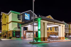 Un hotel con el letrero "Quality Inn & Suites", que cuenta con una entrada cubierta, un estacionamiento y una fachada bien iluminada.