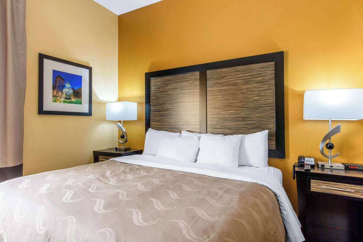 A hotel room with a large bed, two bedside tables, a framed picture on the wall, and a lamp on each side of the bed.
