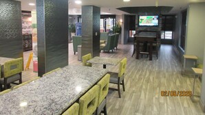 A modern restaurant with high tables and chairs, a TV screen, and a wooden floor. - Quality Inn & Suites Montgomery East Carmichael Rd (Montgomery)