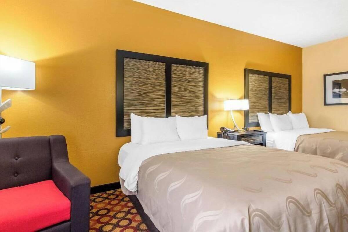 A hotel room with two beds, a sofa, a lamp, and a framed picture on the wall.