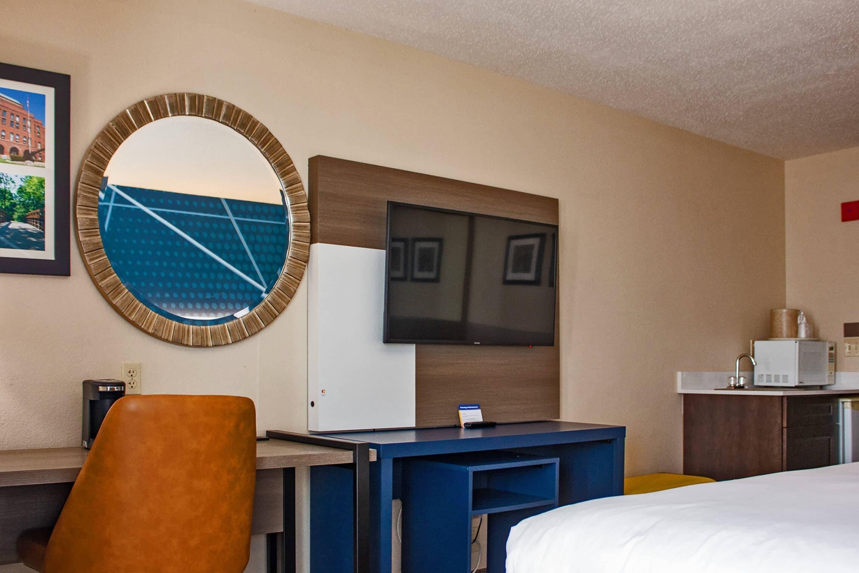 Habitación de hotel con cama, escritorio con silla, televisión, microondas y cafetera.