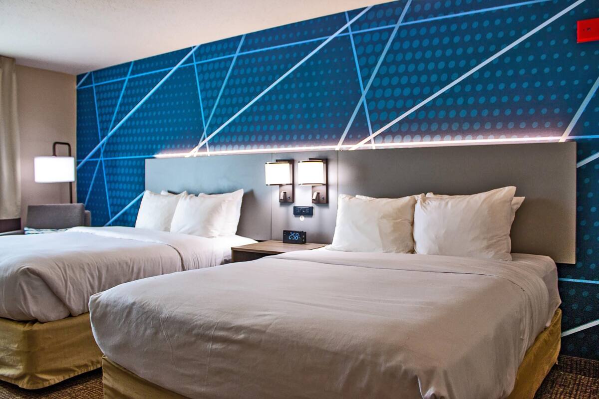 Een hotelkamer met twee bedden, een nachtkastje met een klok en een muur met een geometrisch patroon.