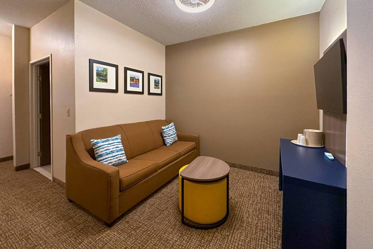 Een hotelkamer met een bruine bank, een klein rond tafeltje en een flatscreen televisie op een standaard.