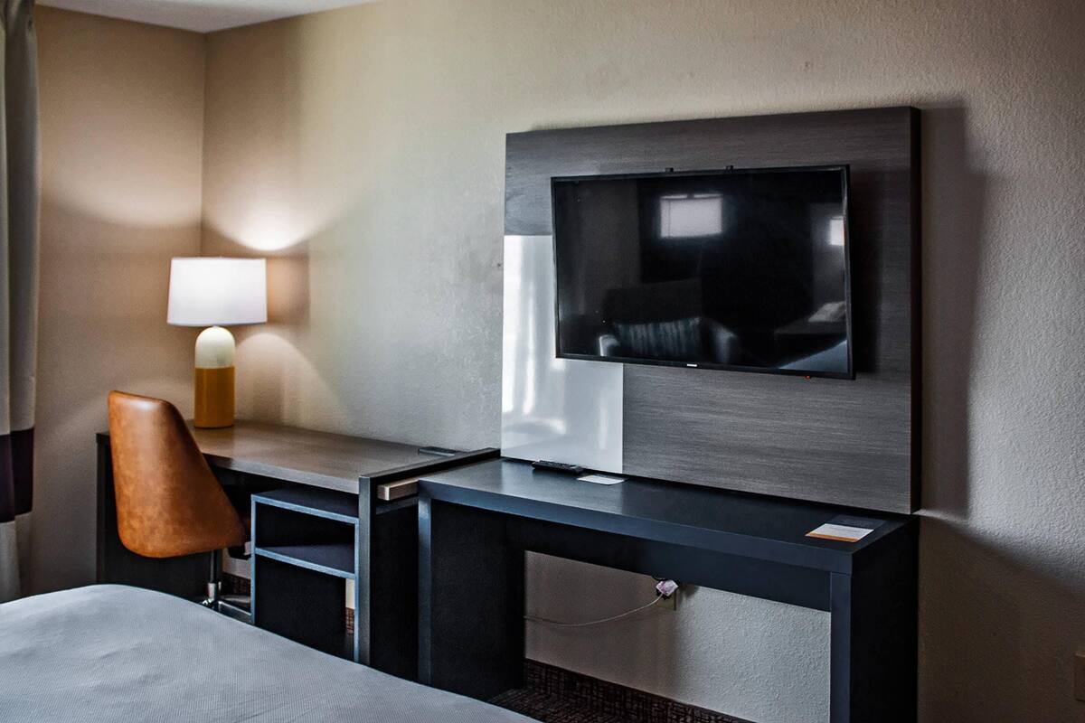 Een hotelkamer met een bed, een bureau met een flatscreen-tv, een lamp en een stoel.