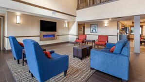 Eine geräumige Lobby mit blauen Sofas, roten Sesseln und einem an der Wand montierten Flachbildfernseher.
