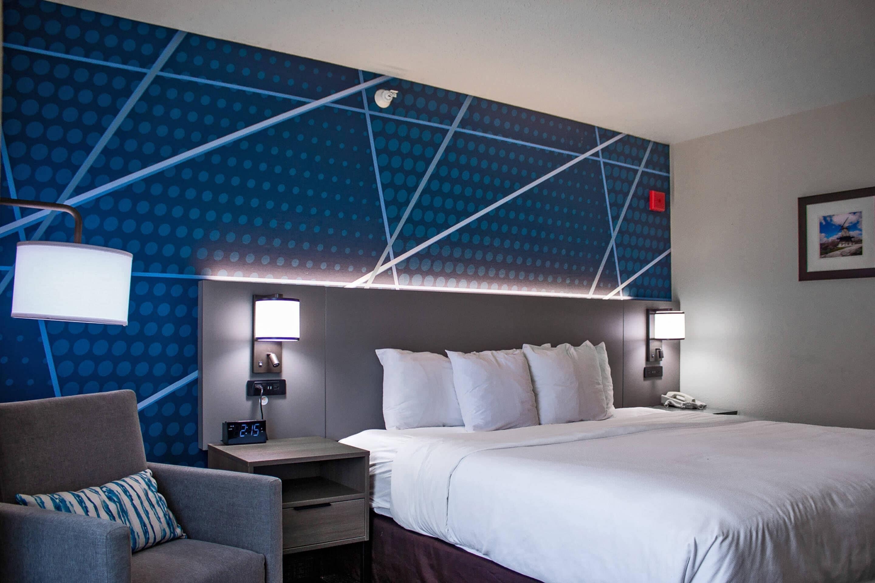 Habitación de hotel con una cama grande, una silla, un escritorio y una pared con un diseño geométrico.