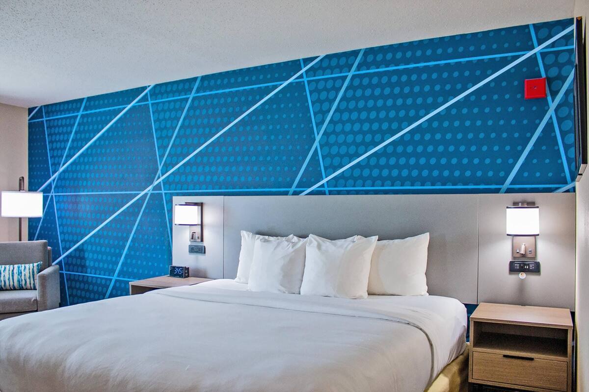 Hotelkamer met een groot bed, twee nachtkastjes, een stoel en een blauwe, gestreept muur.