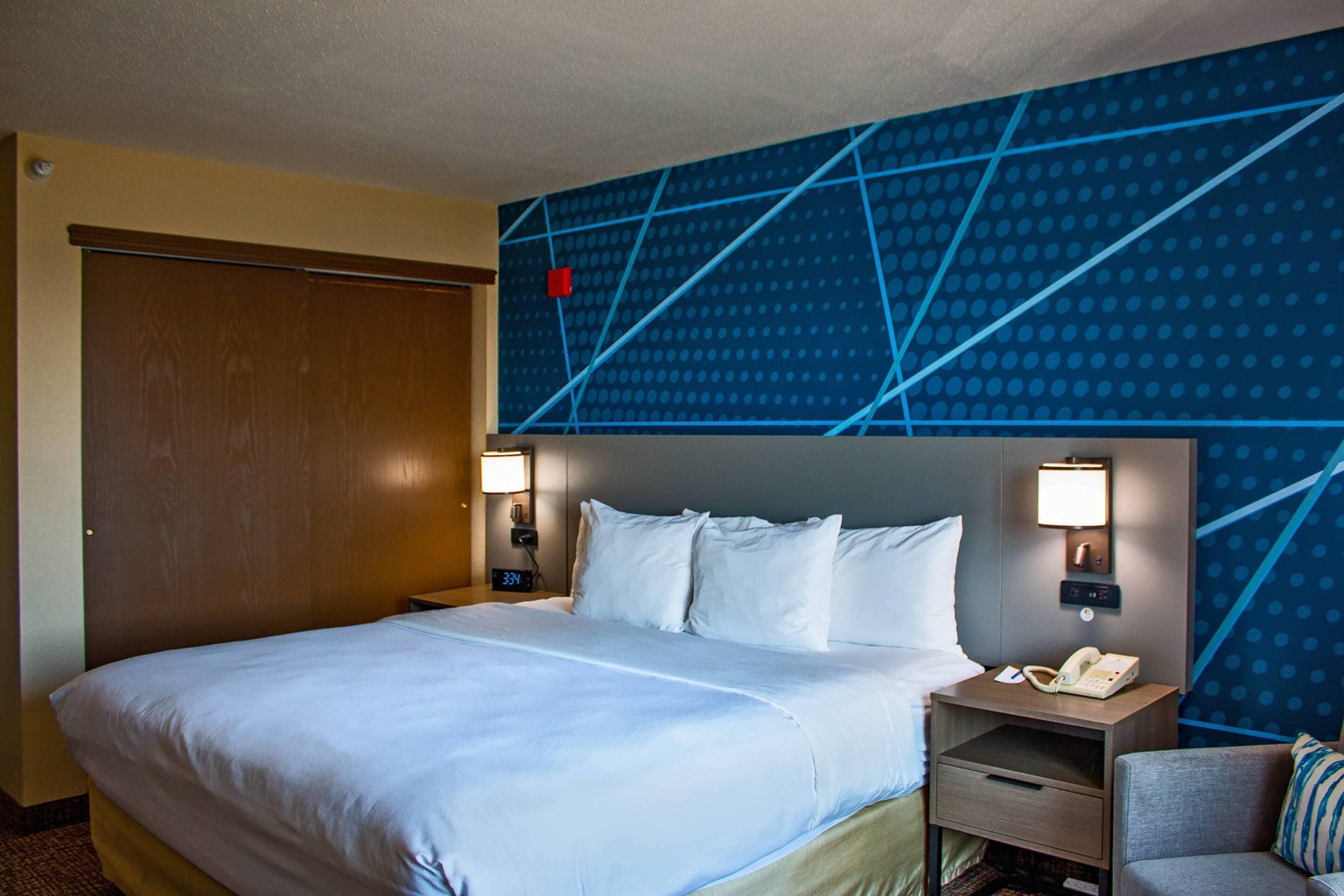 A hotel room with a large bed, two bedside tables with lamps, a nightstand with a telephone, and a blue patterned wall.