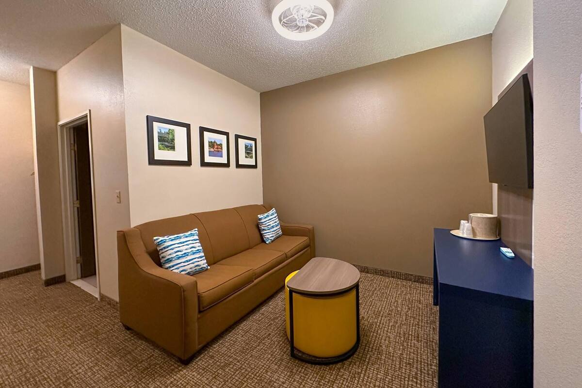 Een hotelkamer met een bruine bank, een klein rond tafeltje en een flatscreen televisie op een standaard.