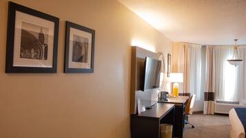 A hotel room with a bed, a desk with a computer, a TV, and two framed pictures on the wall.