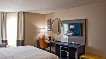 A hotel room with a large bed, a desk with a lamp, a television, and a mirror.