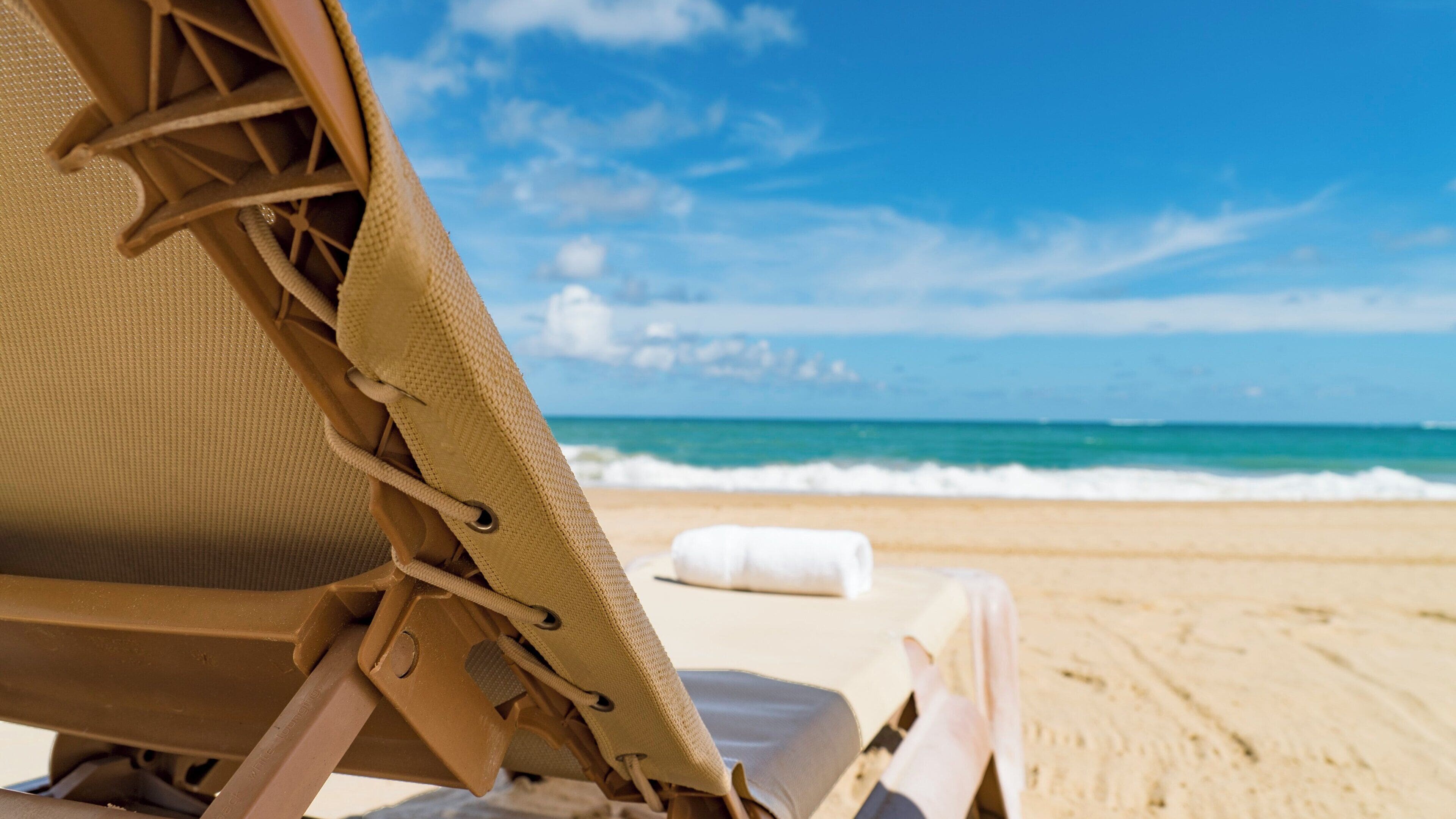 A beach chair with a view of the ocean and a towel on the sand.