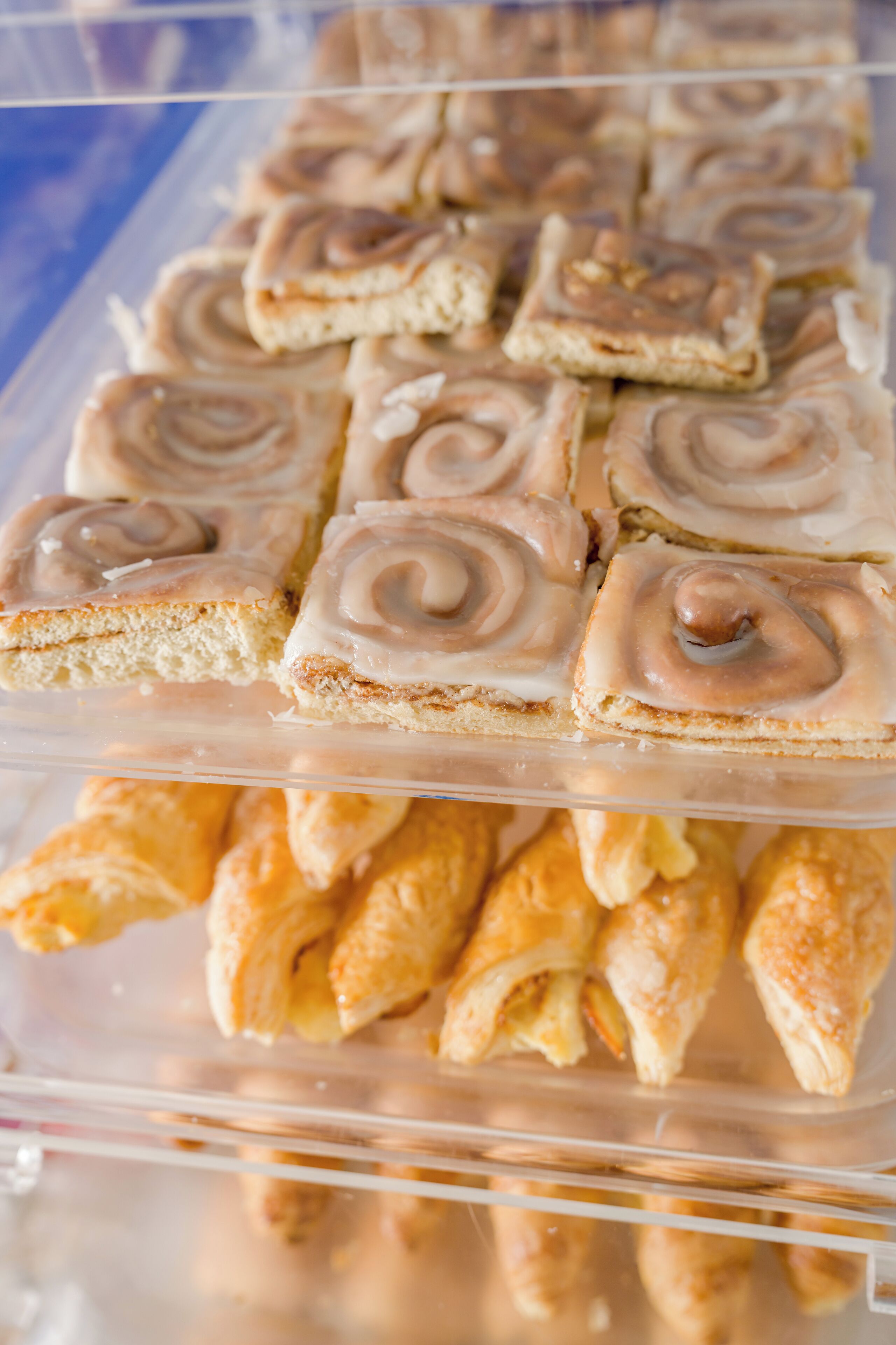 A display of pastries, including cinnamon rolls and croissants, arranged in a clear plastic container.