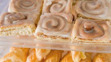 A display of pastries, including cinnamon rolls and croissants, arranged in a clear plastic container.