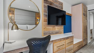 Un dormitorio moderno con cabecera de madera, un espejo grande, un escritorio con lámpara y almacenamiento integrado.