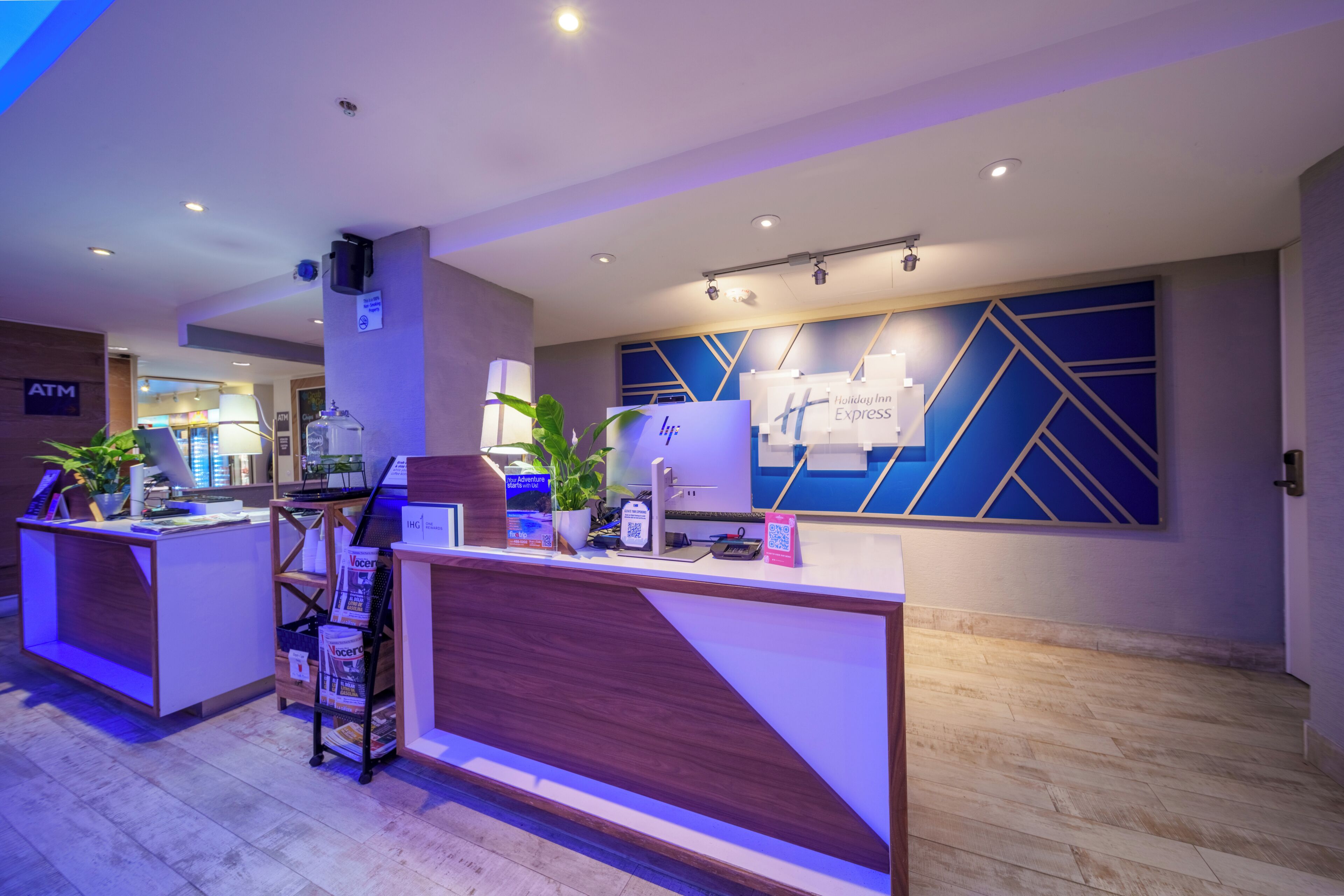 Un'area reception di un hotel con una scrivania in legno, un motivo geometrico blu sul muro e un bancomat.
