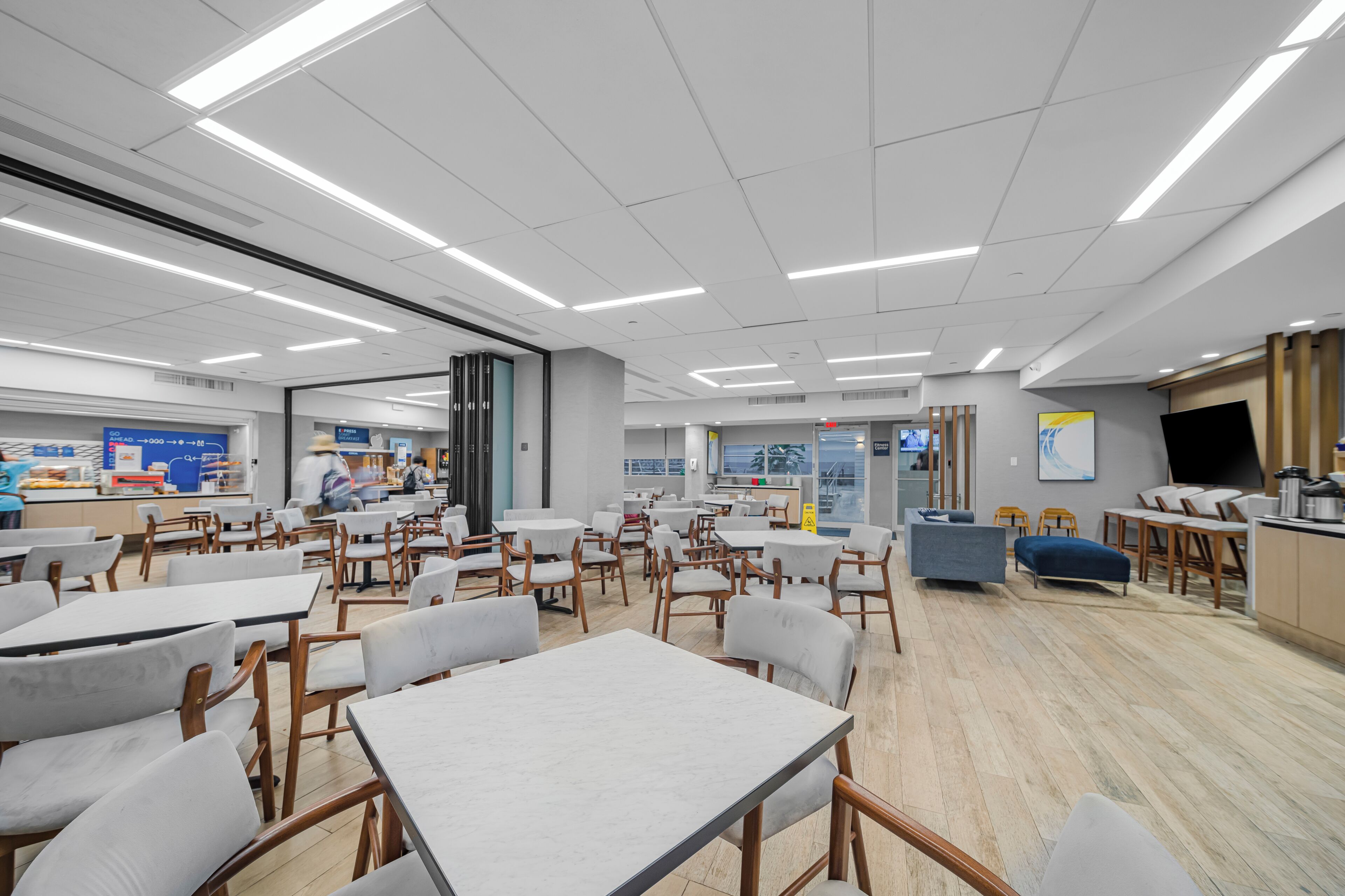 Un espace intérieur spacieux, doté de plusieurs tables et chaises, d’un comptoir et d’un grand écran.
