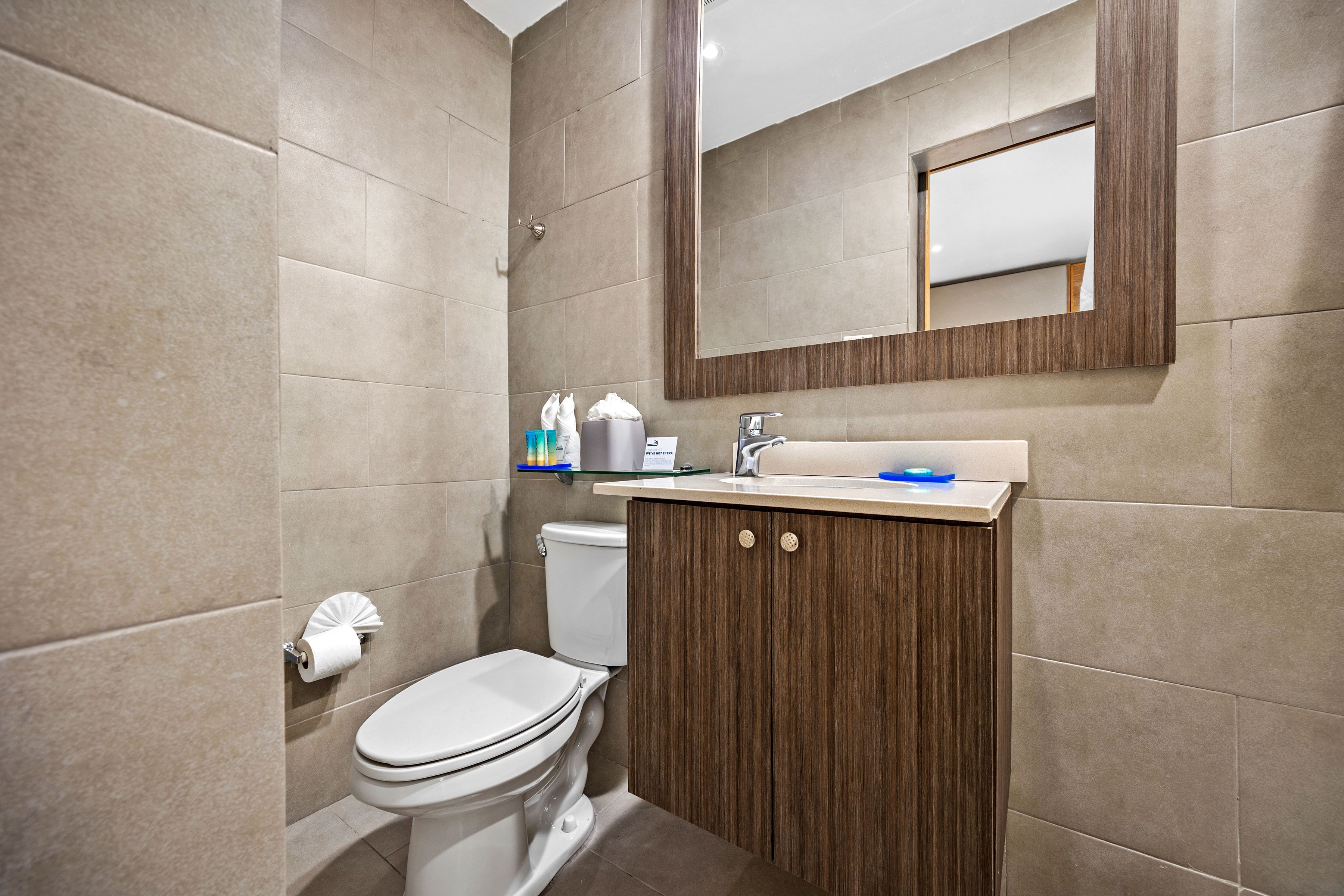 Ein modernes Badezimmer mit Toilette, Waschbecken, Spiegel und beigen Fliesen.