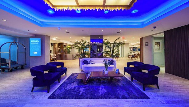 A modern lobby with a white sofa, dark armchairs, a wooden coffee table, and a blue-lit ceiling. - Holiday Inn Express San Juan Condado by IHG (San Juan)