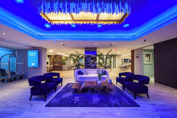 A modern lobby with a white sofa, dark armchairs, a wooden coffee table, and a blue-lit ceiling. - Holiday Inn Express San Juan Condado by IHG (San Juan)