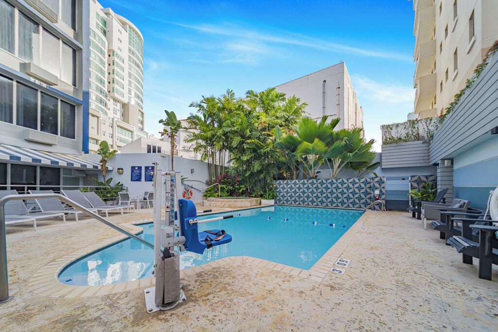 A swimming pool with lounge chairs, surrounded by buildings and palm trees.