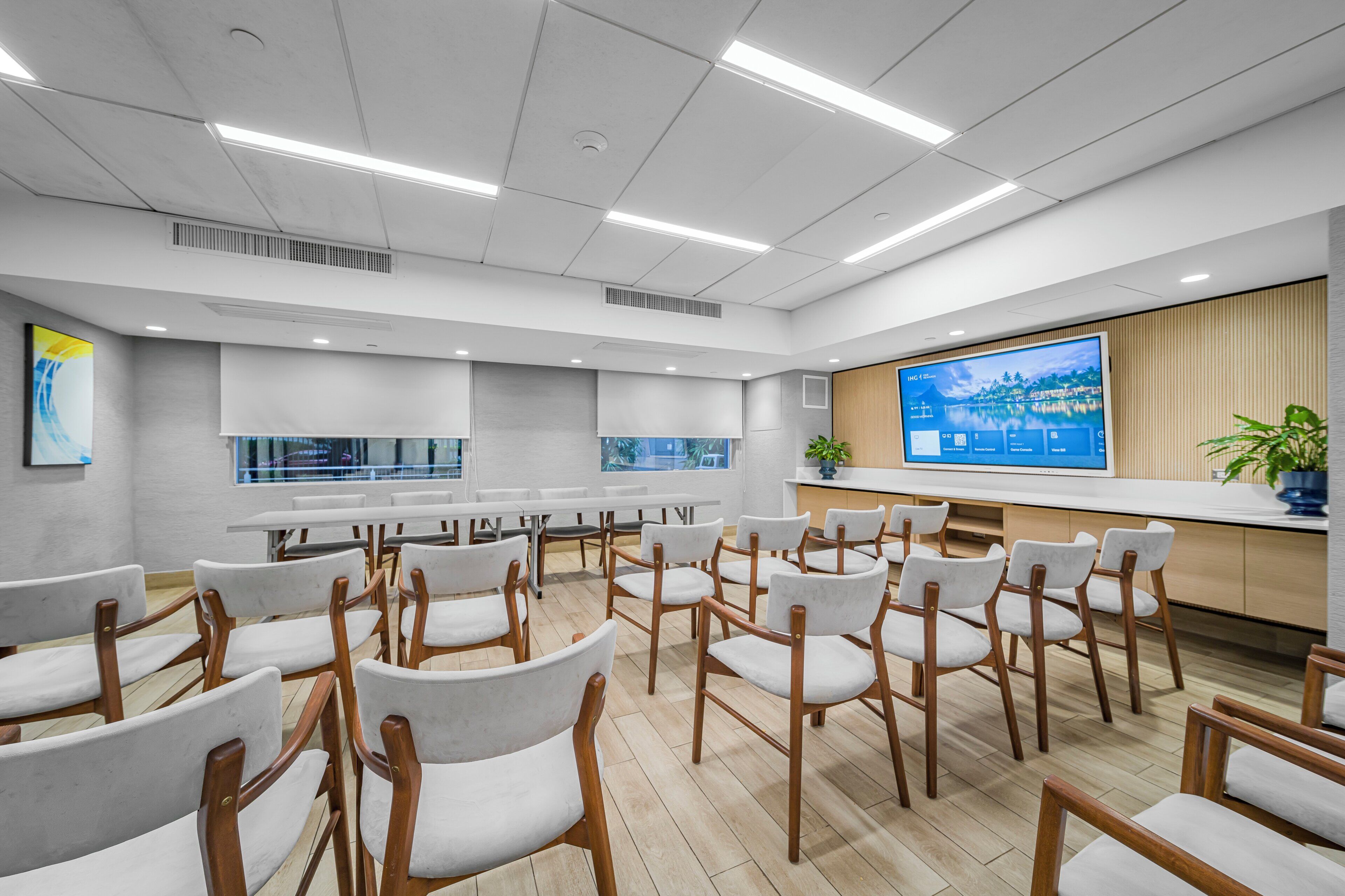 A conference room with white chairs, a large screen, and a wooden counter.