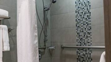 A modern shower area with a glass door, a tiled wall with a mosaic pattern, and a handrail.