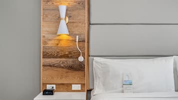 A neatly made bed with white linens, a bedside table with a digital clock, a wall-mounted lamp, and a wooden panel design.