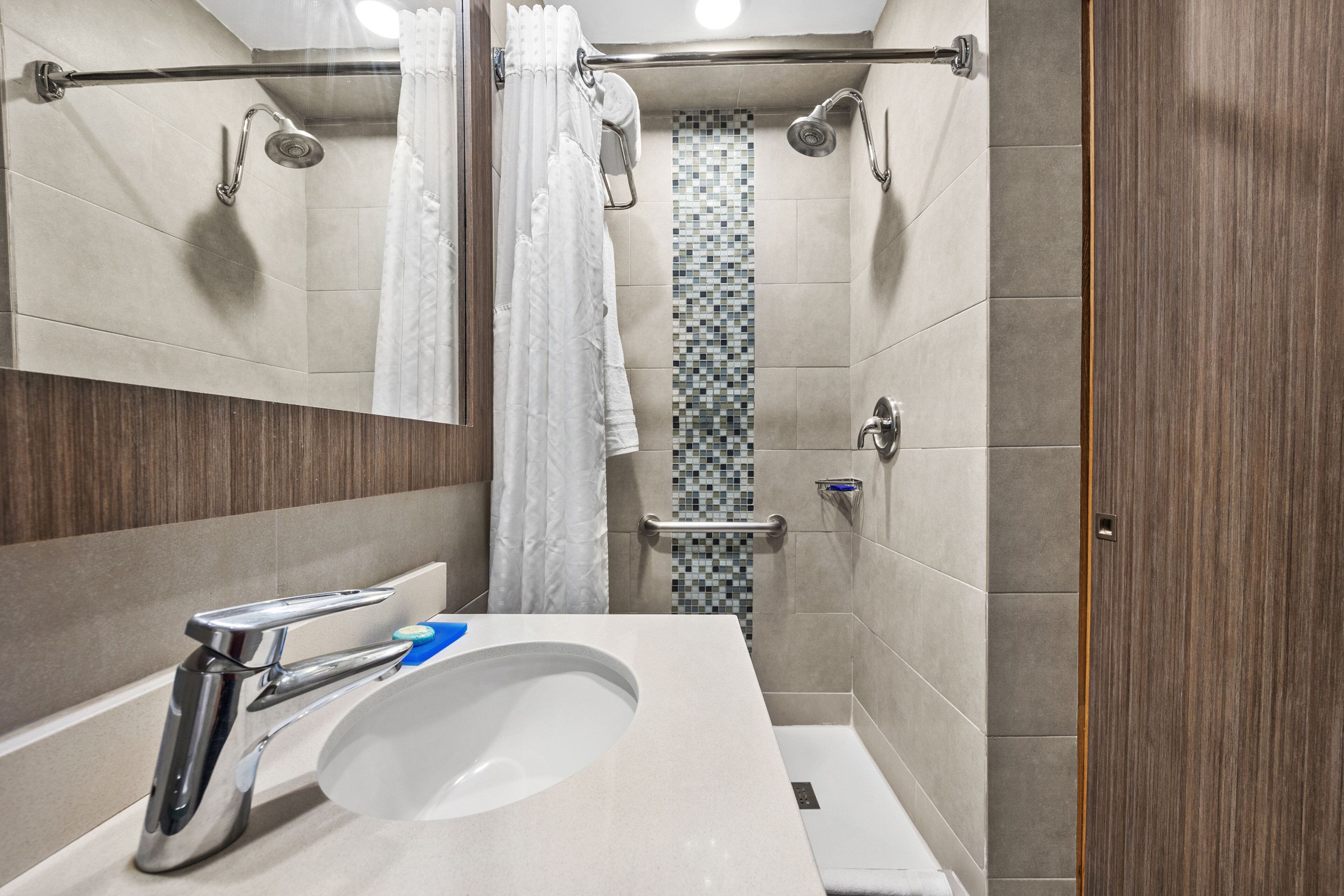 A modern bathroom with a sink, mirror, shower, and tiled walls.