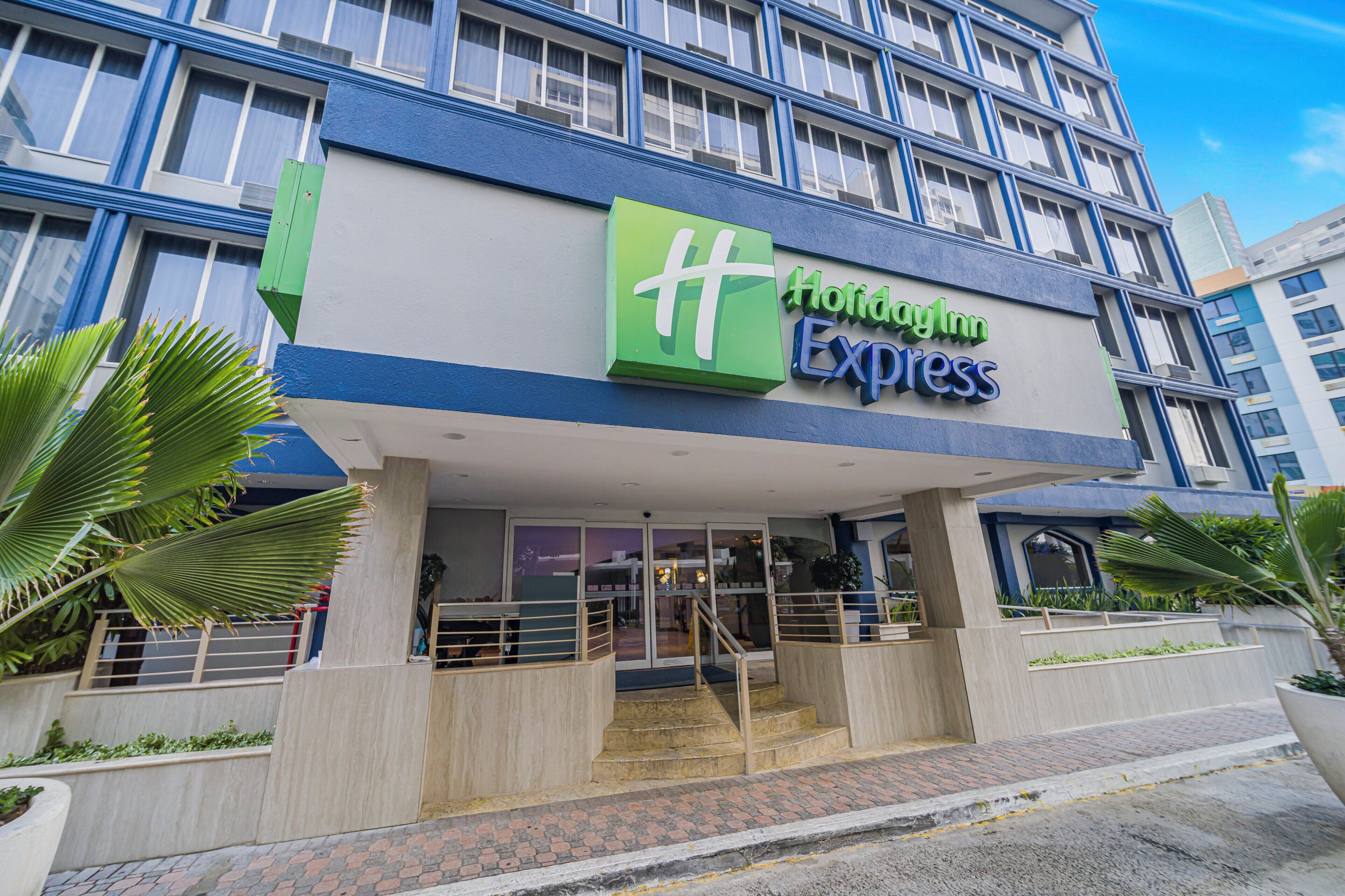 A hotel with a prominent green and blue sign, a modern facade, and a staircase leading to the entrance.