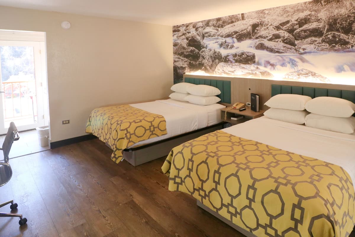 Une chambre d’hôtel avec deux lits, un plancher en bois, une grande fenêtre et une fresque murale.